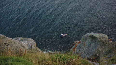 High-angle view from a rocky cliff looking down at a small fishing boat in the 스톡 동영상 344212168