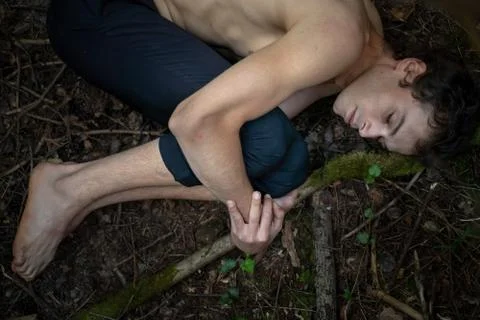 High angle view of shirtless man with eyes closed hugging knees while lying on Stock Photos