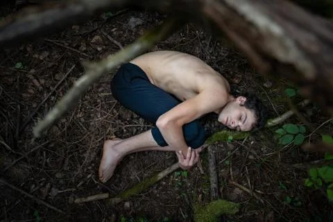 High angle view of shirtless man hugging knees while sleeping on dirty land in Stock Photos