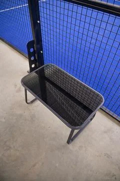 High-angle view of a small black glass bench situated next to a blue sports.. Stock Photos
