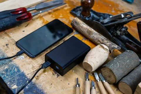 High-Angle View of Smartphone Charging on Woodworking Workbench Stock Photos