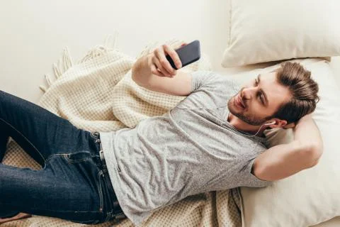 High angle view of smiling handsome young man in earphones using smartphone a Stock Photos