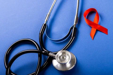 High angle view of stethoscope with red aids awareness ribbon against blue Stock Photos