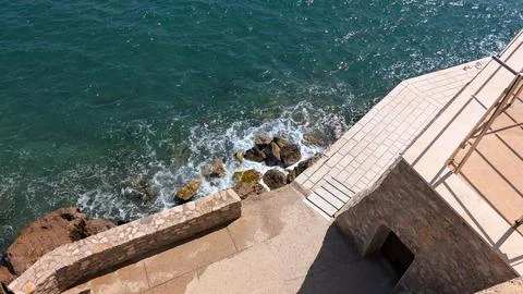 High angle view of a stone promenade next to the turquoise sea with splashi.. Photos