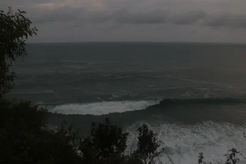 High angle view through trees on to the ocean with big waves and cloud sky Stock Photos