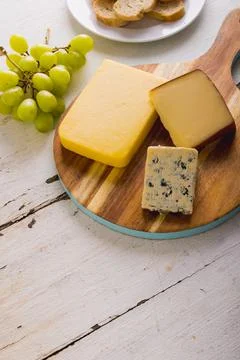 High angle view of various cheese on wooden board by grapes on table, copy space Stock Photos