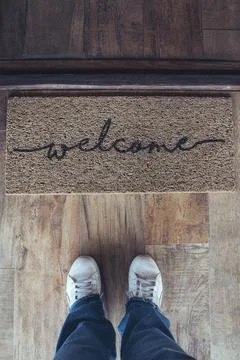 High angle view of welcome mat in door over wooden floor with woman foot ware Stock Photos