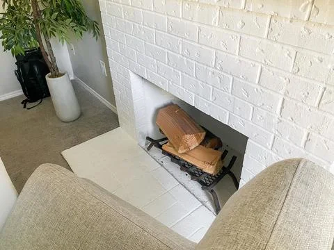 A high-angle view of a white brick fireplace with logs, framed by two beige a Stock Photos