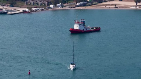 High angle view of a white sailboat sailing on calm blue sea water past a red Stock Footage 346745411