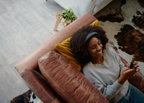 High angle view of woman lying on couch and listening to music using and typing Stock Photos