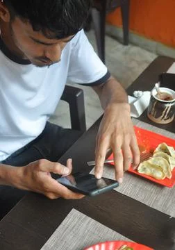 High angle view of a young guy using phone during eating fast food in the cafe Stock Photos