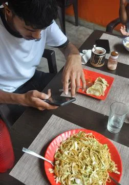 High angle view of a young guy using phone during eating fast food in the cafe Stock Photos