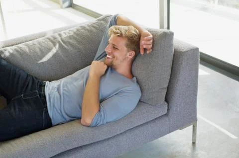 High angle view of a young man lying on a couch at home and smiling Stock Photos