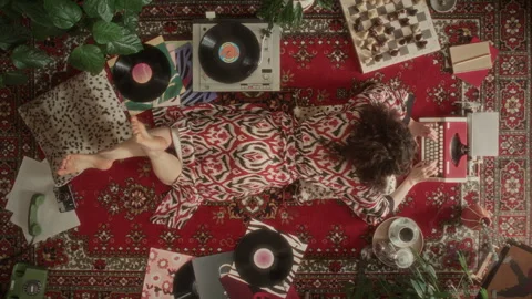 High Angle of Woman in Robe Lying on Rug, Using Typewriter and Enjoying Music Stock Footage 339852513