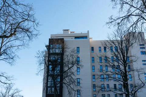 High apartment building surrounded by trees without leaves against a blue sky Stock Photos