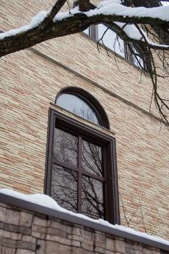 High arched window in brick wall with reflection of bare branches, snow on tr Stock Photos
