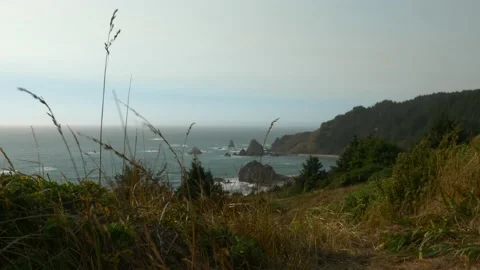 High up on a beach cliff, ocean down below with large rocks and grassy hills Stock Footage 162767141