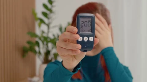 High blood sugar reading of 200 mg dL shown by a woman in a living room Stock Footage 334034569