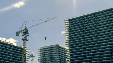 High building under construction. Side with cranes against blue sky with sun Ilustración de archivo
