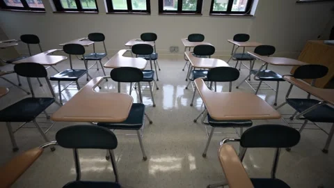 High camera pushes toward back of room through a row of empty desks chairs in a Stock Footage 247525021