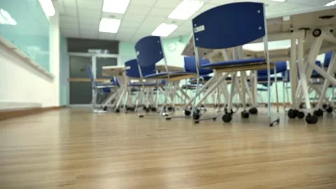 High camera pushes toward back of room through a row of empty desks chairs in Stock Footage 256720546