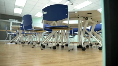 High camera pushes toward back of room through a row of empty desks chairs in Stock Footage 256720613