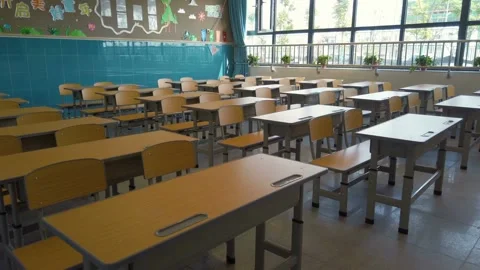 High camera pushes toward back of room through a row of empty desks chairs in Stock Footage 256721029