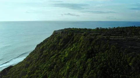 High cliffs with many green trees with peaceful blue sea surface Stock Photos