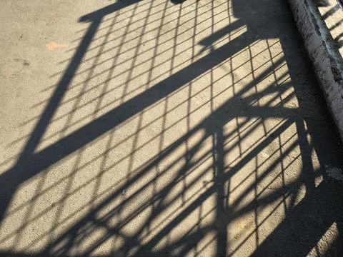 High contrast geometric grid shadow cast on textured concrete ground. Stock-Fotos