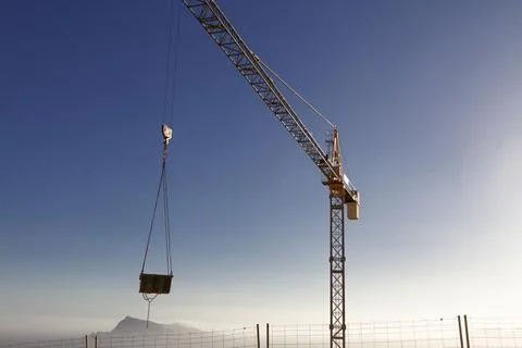 High crane lifting cargo on a background of sky and mountains. Stock Photos