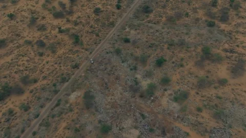 High drone view of a lone 4x4 on a narrow dirt track through rocky scrubland in Stock Footage 345845503