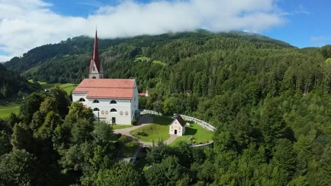High elevation view historic church with tall spire framed by dense forest and 스톡 동영상 325753657