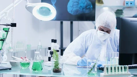 In high-end biochemistry laboratory a scientist in coveralls is making notes Video stock 113672492
