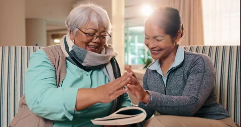 High five, book and nurse with old woman on sofa for crossword puzzle, support Stock Footage 341387208