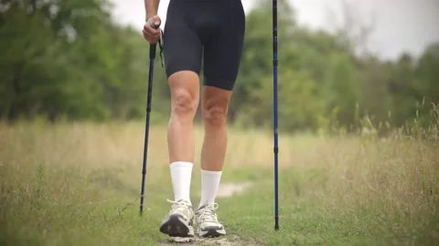 High-knee warm-up with walking poles on grassy trail through meadow Stock Footage 313951330