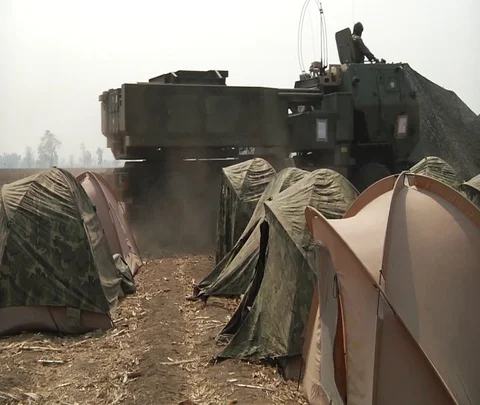High mobility artillery rocket system being driven past tents at base camp Stock Footage 102944299