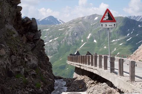 High mountain road with falling rock warning sign Stock Photos