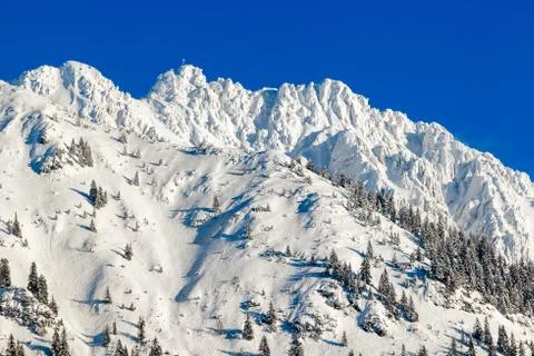 High mountain with summit cross under deep snow in winter. Rauhhorn, Allgau Stock Photos