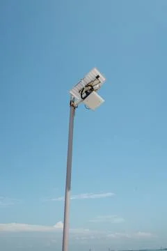High pole supports large, angled light fixture against clear sky Stock Photos