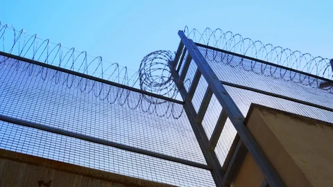High prison fence with barbed wire, bottom view. Prison fence against clear sky. Stock Footage