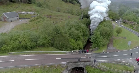 High pull back aerial shot of the Jacobite Express leaving Glenfinnan Video stock 169062568