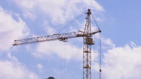 A high-rise construction crane turns against a background of blue sky and clouds Stockbeeldmateriaal 136696975