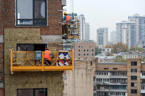 High rise construction work. Construction site workers in cradles working wit Stock Photos