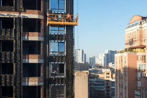 High rise construction work. Construction site workers in cradles working wit Stock Photos