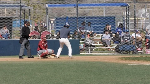 High school baseball player hits ball &amp; runs to first base with catcher Stock Footage 125025856