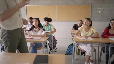 In the high school classroom: An enthusiastic teacher walks among rows of bright Stock Footage