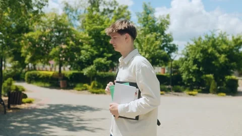 High school student with backpack walks down green schoolyard path Stock Footage 310882526