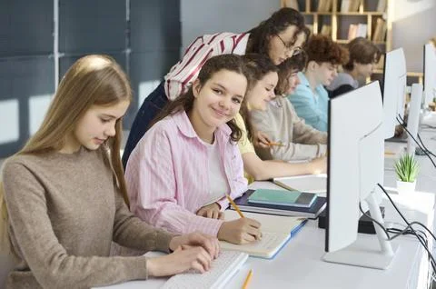 High school students coding at computers with teacher help in modern classroom 库存照片