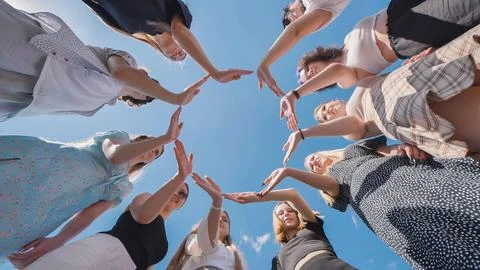 High school students joining hands in a circle under a vibrant blue sky Photos