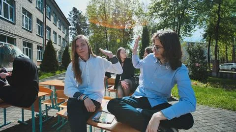 High school students taking a break outdoors, sitting on desks and enjoying Stock Photos